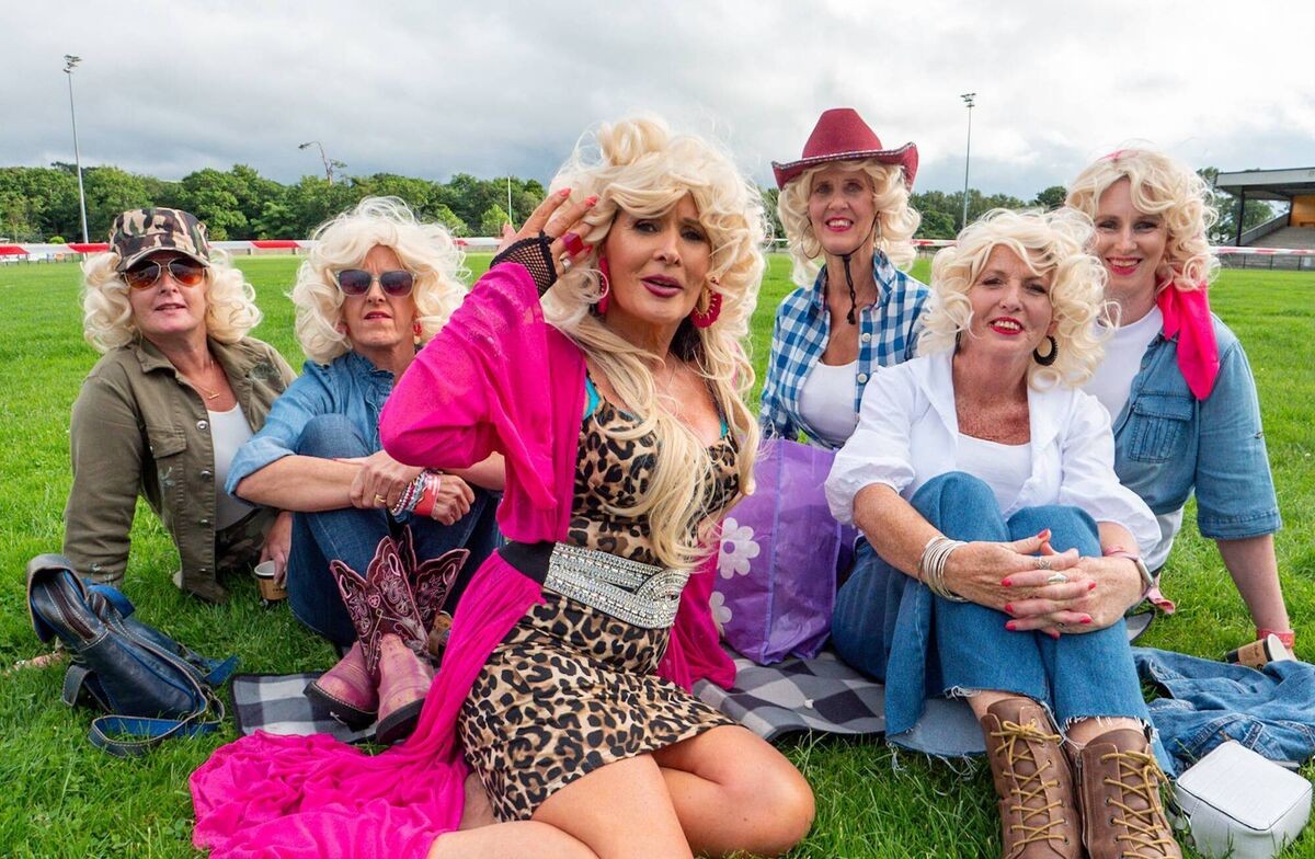 A group in wigs and cowboy hats sitting together on the grass